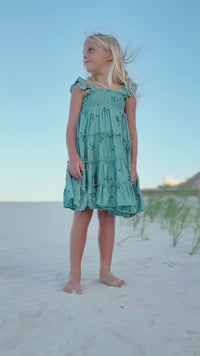 SS Girl's Dress Pia Dress (jade bloom). Girl wearing Indie Blue Pia Dress in Jade Bloom twirling on the beach