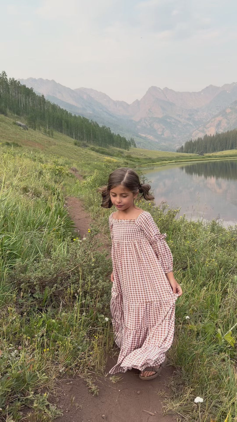 SS Girl's Dress Pippa Maxi (brown gingham) Girl wearing Indie Blue Pippa Maxi Dress in Brown Gingham walking by a lake with mountain backdrop